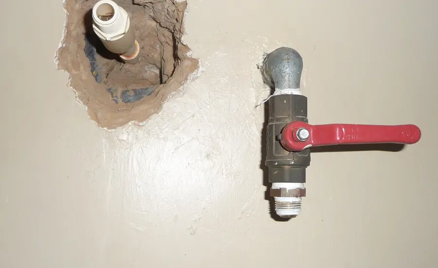 Absperrhahn mit rotem Hebel an einer Wasserleitung neben einer offenen Wandaussparung