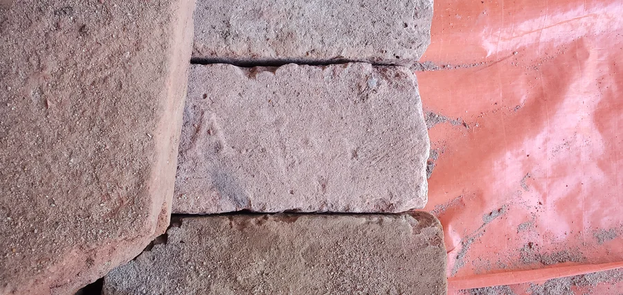 Nahaufnahme alter roter Ziegel mit Mörtelresten und unregelmäßigen Kanten.