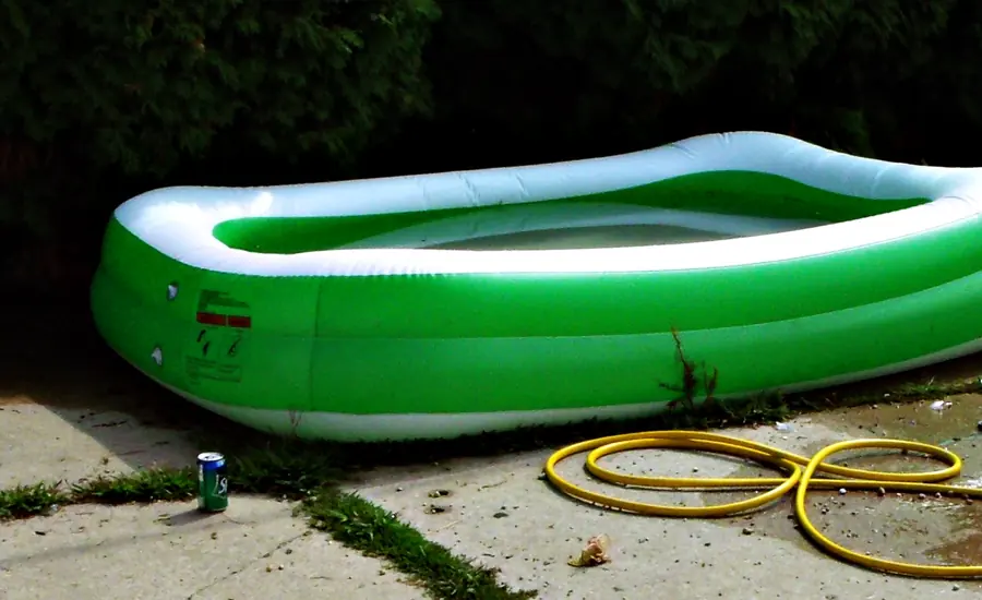 Grün-weißer aufblasbarer Pool auf einer Betonterrasse neben einem gelben Gartenschlauch