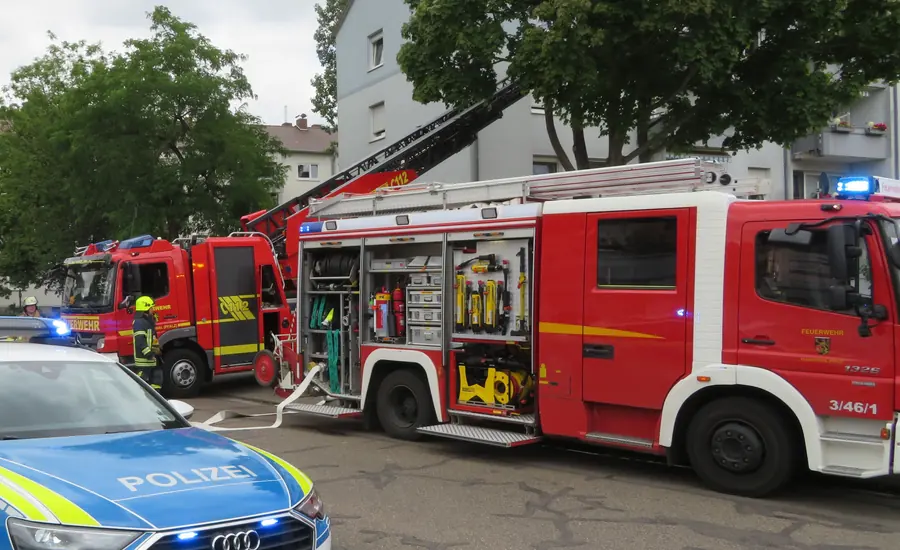 Feuerwehreinsatz vor einem Wohnhaus: Löschfahrzeug mit geöffneten Geräteräumen und ausgelegtem Schlauch, dahinter die Drehleiter, vorn ein Streifenwagen der Polizei