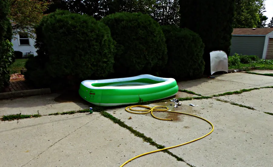 Kleiner grüner Aufstellpool aus Kunststoff auf einer Terrasse mit Gartenschlauch