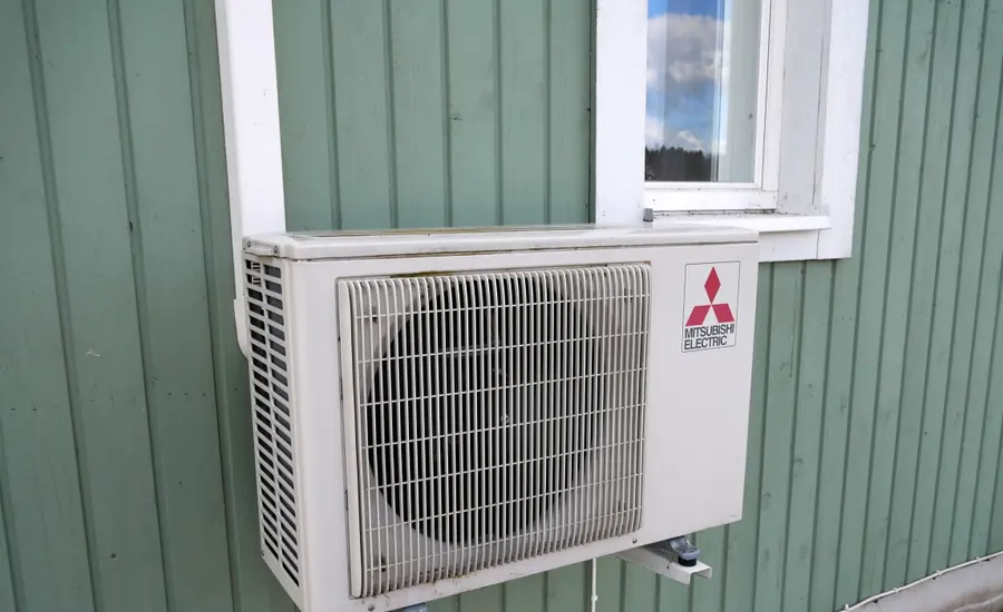 Weißes Außengerät einer Split-Klimaanlage an einer grün gestrichenen Holzfassade