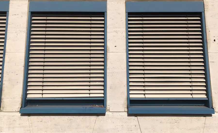 Zwei Fenster mit heruntergelassenen Außenjalousien an einer hellen Fassade