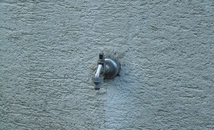 Außenwasserhahn mit Schlauchanschluss an einer grob verputzten Hauswand
