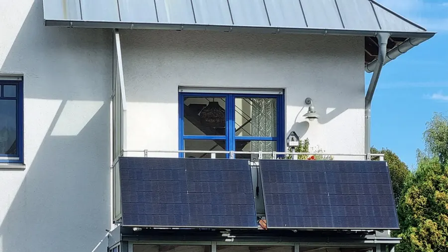 Zwei Solarmodule an der Brüstung eines Balkons an einem Wohnhaus mit Metalldach