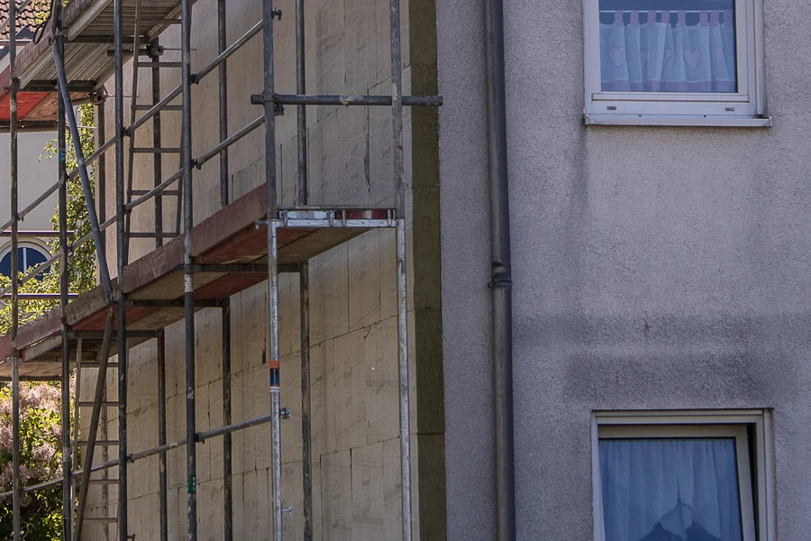 Baugerüst vor einer Hausfassade mit Dämmplatten und angrenzenden Fenstern