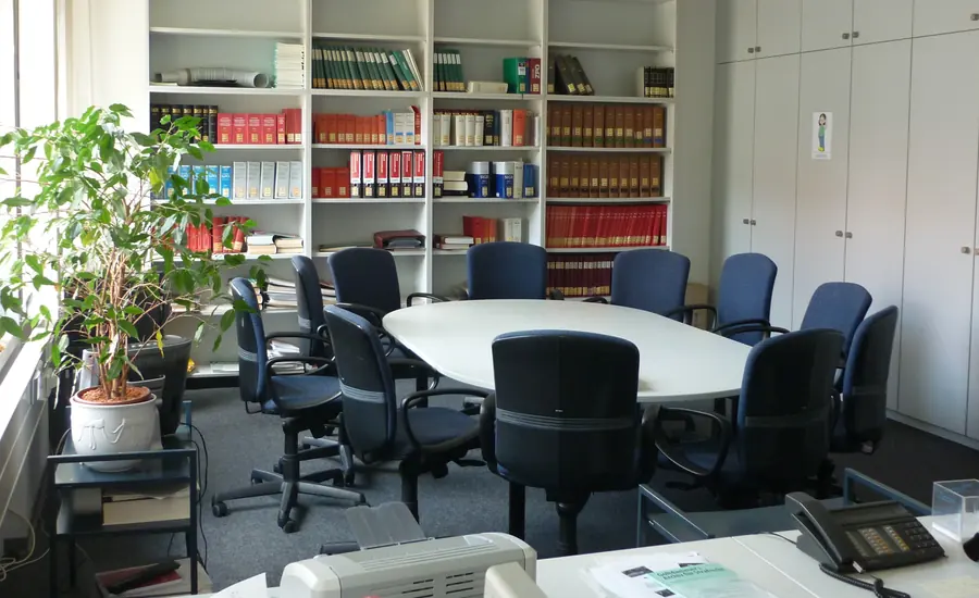 Beratungszimmer mit ovalem Tisch, ringsum angeordneten Stühlen und Regalen voller gebundener Gesetzesbände