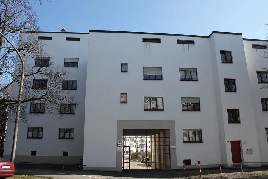 Weiß verputzte Fassade einer mehrgeschossigen Wohnanlage mit Toreinfahrt