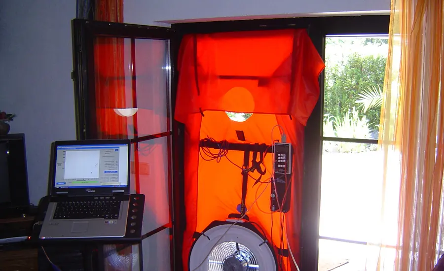Rote Blower-Door-Messeinrichtung in einer Türöffnung, davor ein Laptop mit Messsoftware