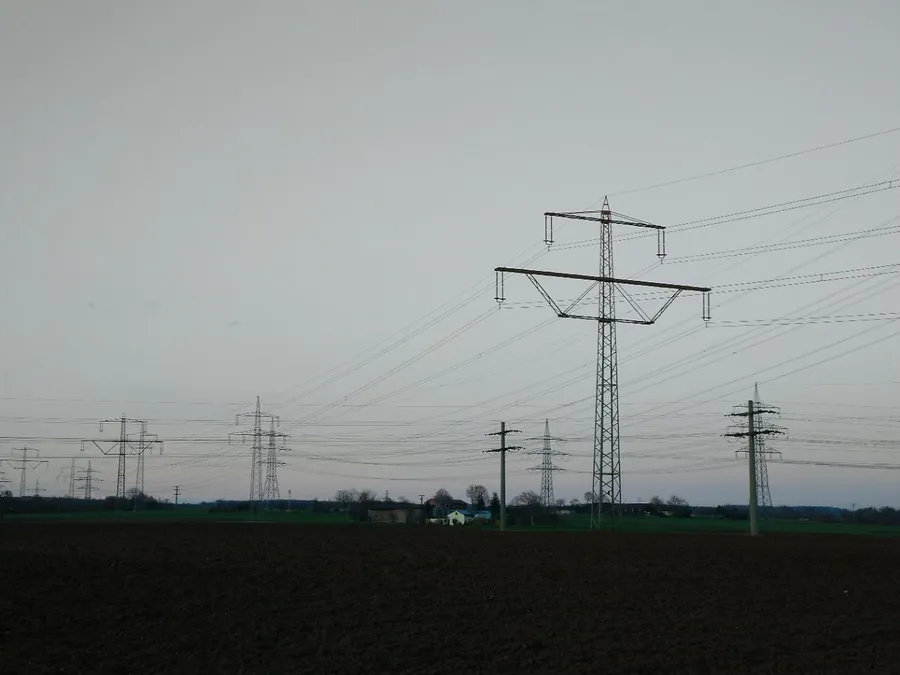 Hochspannungsmasten und Stromleitungen über einem Feld
