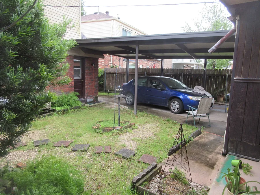 Carport mit flachem Dach an einem Wohnhaus, darunter ein blauer Pkw