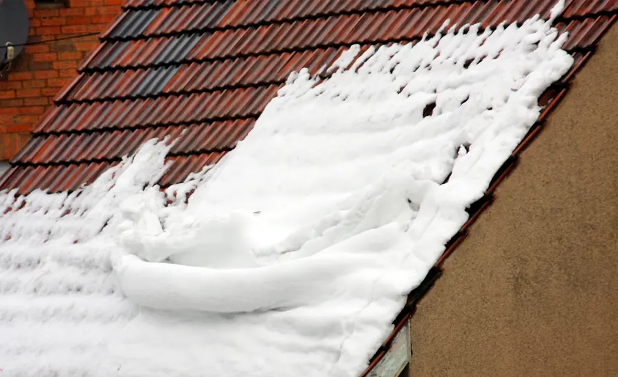 Zusammengeschobene Schneeschicht auf den roten Ziegeln eines Steildachs