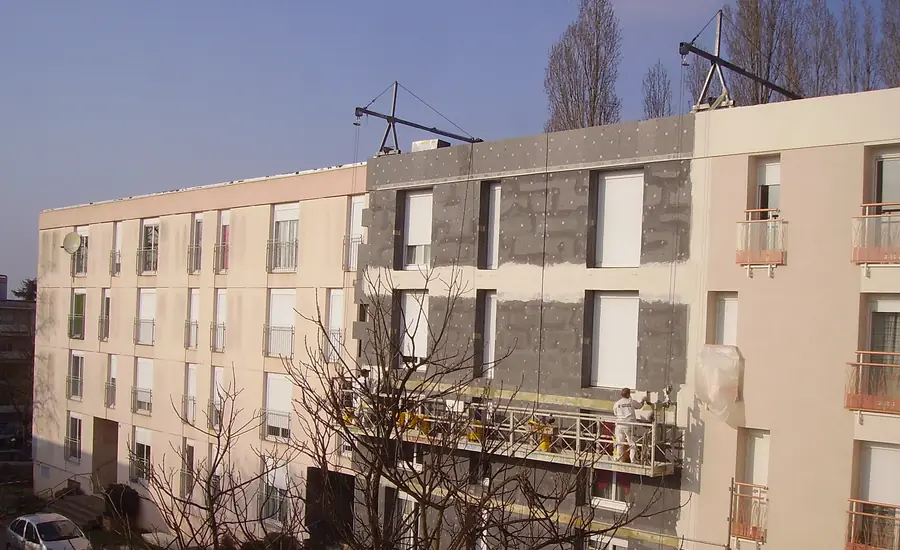 Fassade eines mehrgeschossigen Wohnhauses mit montierten Dämmplatten und teilweise aufgetragenem Putz