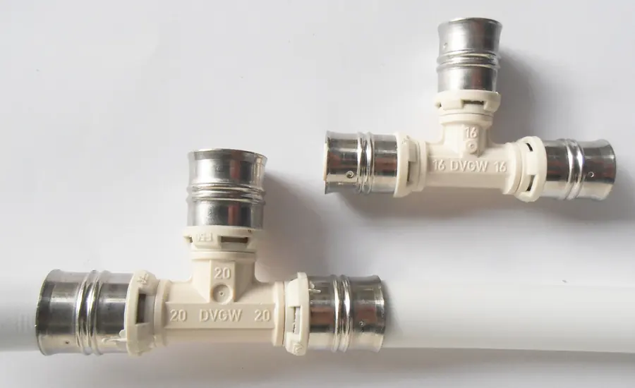 Zwei T-Pressfittings mit DVGW-Prägung in 20 und 16 Millimeter Nennweite mit Edelstahl-Presshülsen, darunter ein weißes Mehrschichtverbundrohr