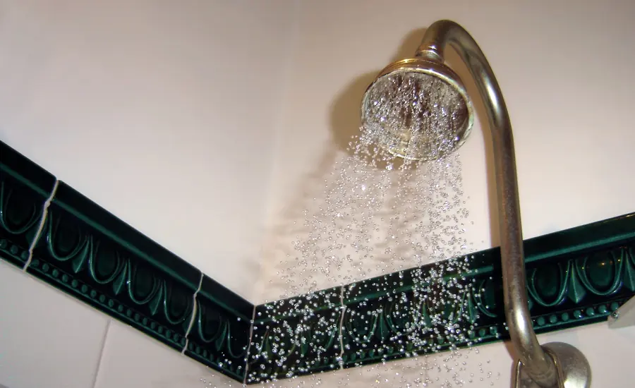 Goldfarbener Duschkopf mit laufendem Wasser vor einer gefliesten Badwand