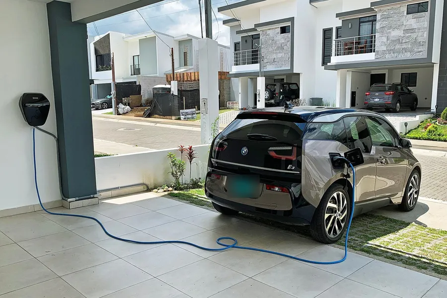 Elektroauto lädt in einer Carport-Einfahrt über eine Wandladestation mit blauem Ladekabel