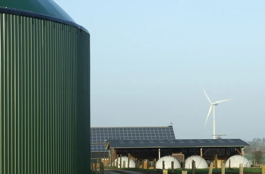 Fermenter einer Biogasanlage mit Solardach auf dem Stall und einem Windrad im Hintergrund