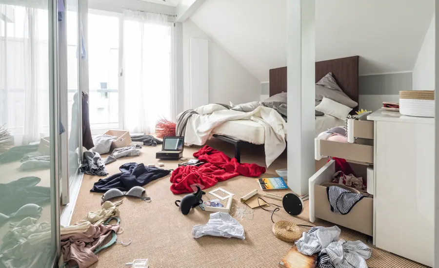 Schlafzimmer nach einem Einbruch mit aufgerissenen Schubladen und Kleidung auf dem Boden