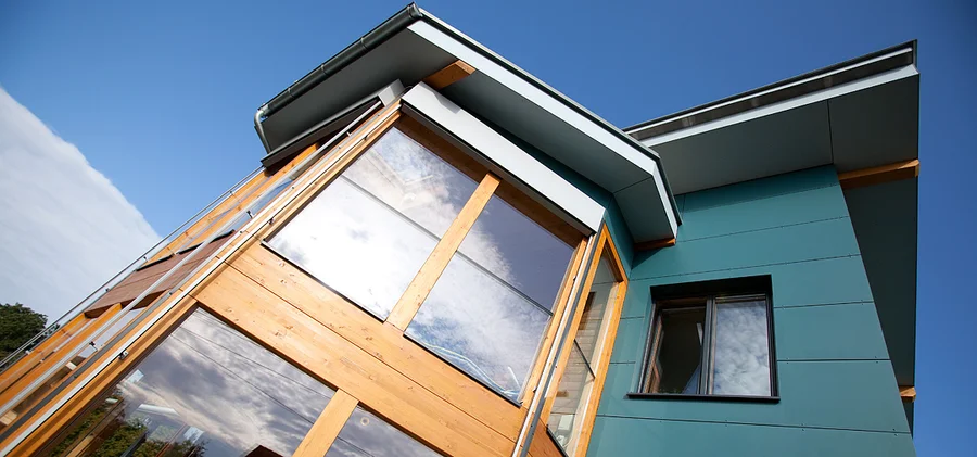 Hausfassade mit großen verglasten Flächen, Holzrahmen und grünlichen Fassadenplatten