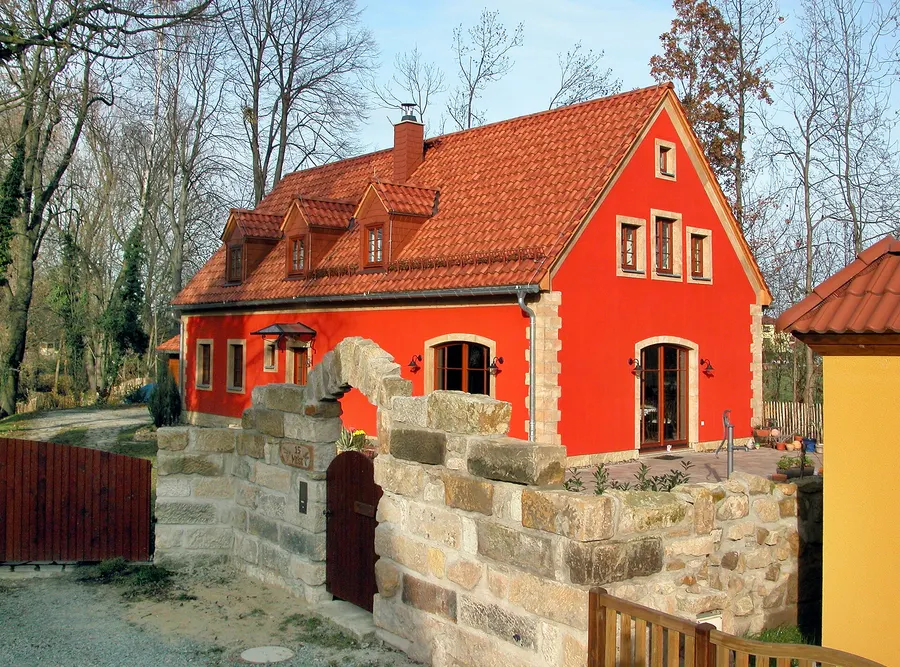 Rot verputztes Wohnhaus mit Ziegeldach und Gaube hinter einer Natursteinmauer