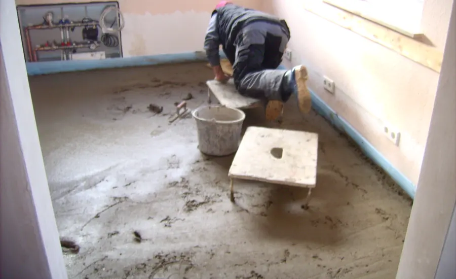 Handwerker glättet frischen Estrich auf dem Boden eines leeren Raums