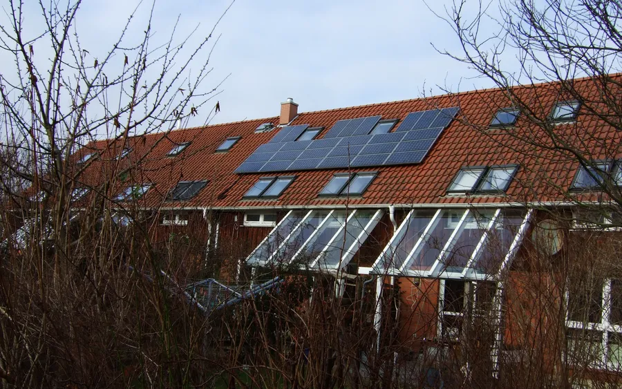 Ziegeldach einer Reihenhauszeile mit Photovoltaikmodulen und Dachfenstern, davor kahle Zweige
