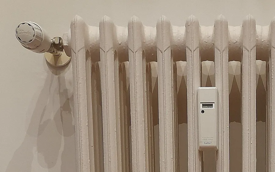 Weißer Gussheizkörper mit Thermostatkopf und Heizkostenverteiler an einer Wand