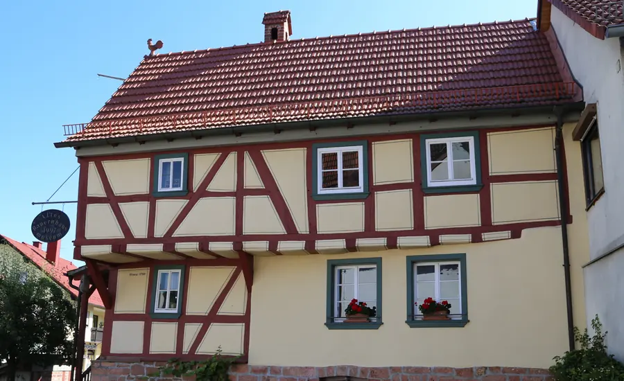 Fachwerkhaus mit rotem Ziegeldach, hellen Gefachen und Fenstern mit Blumenkästen