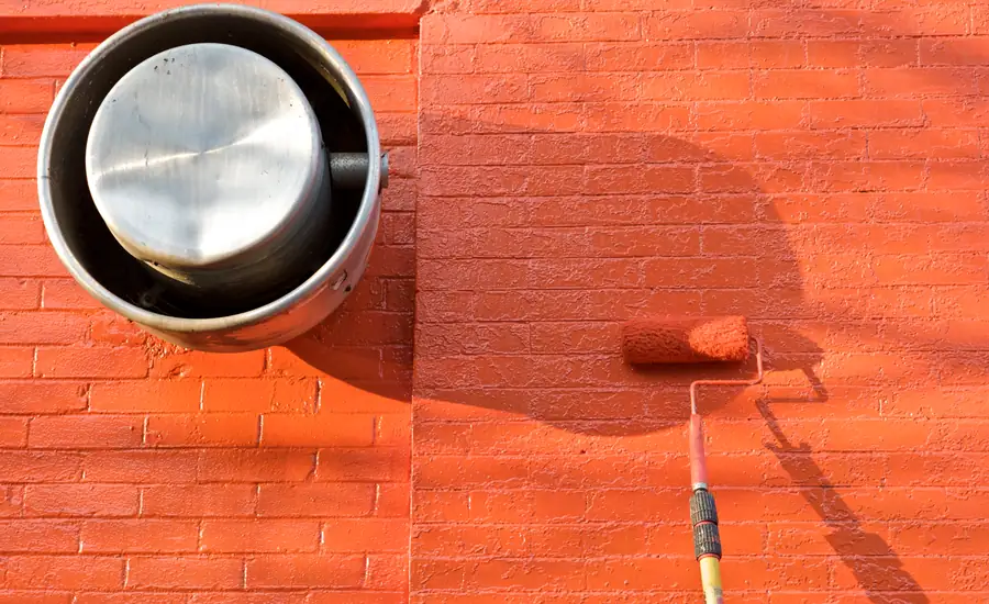 Farbrolle und Farbeimer vor einer orange gestrichenen Wand