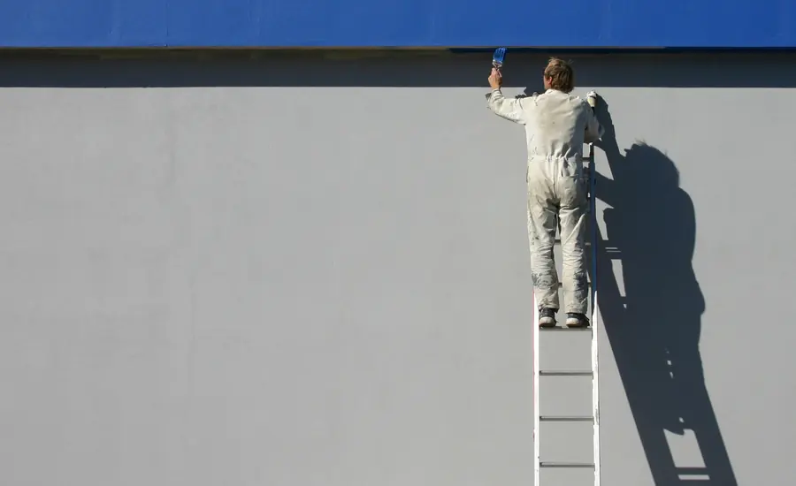 Maler streicht auf einer Leiter stehend eine glatte Hausfassade