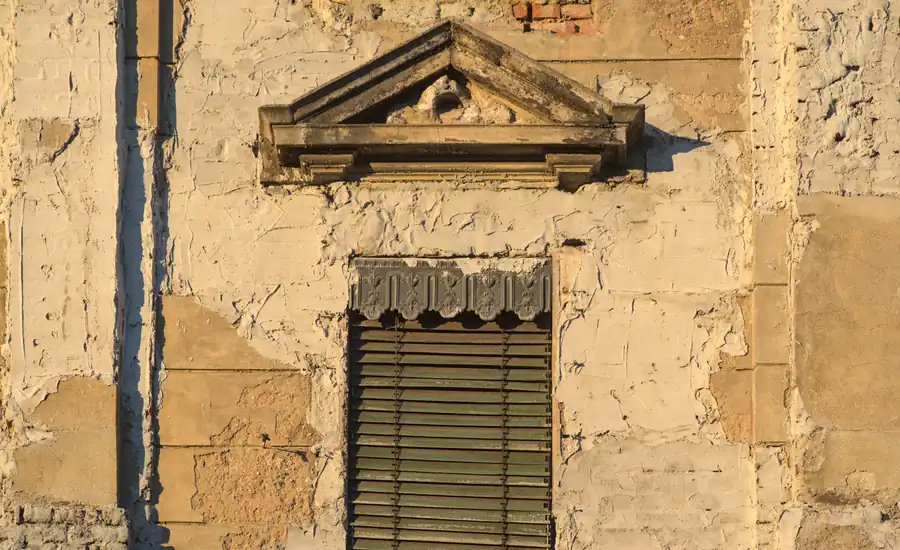 Fenster mit geschlossenem Rollladen und Gesims an einer verwitterten Altbaufassade
