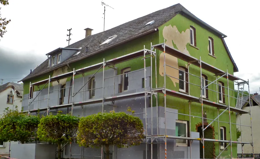 Eingerüstetes Mehrfamilienhaus: An der Fassade sitzen graue Dämmplatten bis an die Fensteröffnungen, darüber ist noch der alte grüne Putz zu sehen