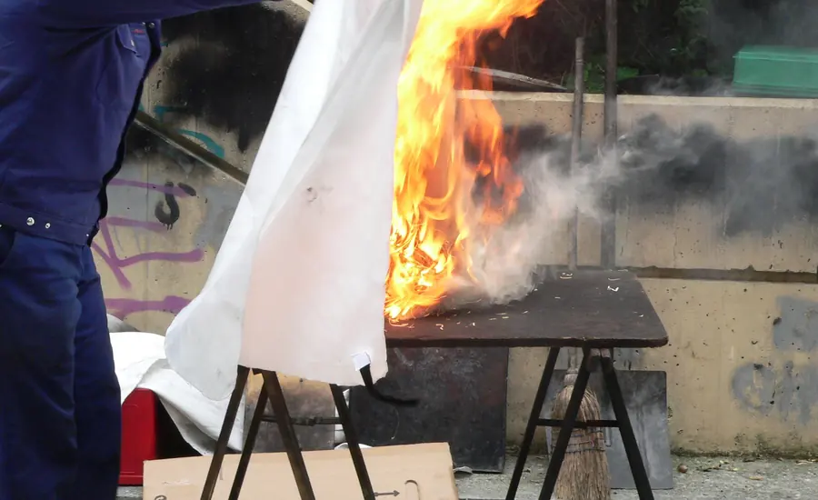 Person erstickt ein Feuer auf einem Tisch mit einer weißen Löschdecke