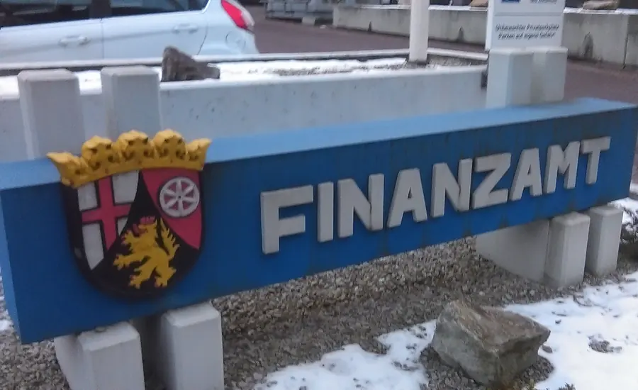 Blaues Schild mit der Aufschrift FINANZAMT und dem Wappen von Rheinland-Pfalz auf einer Mauer, davor Schneereste