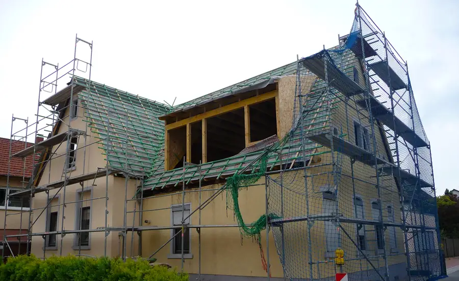 Eingerüstetes Wohnhaus beim Dachausbau: Das Dach ist mit grüner Bahn und Lattung belegt, in der Mitte entsteht eine große Gaube im Holzrahmen