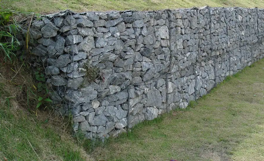Mit grauem Bruchstein gefüllte Gabionenwand entlang einer Rasenböschung