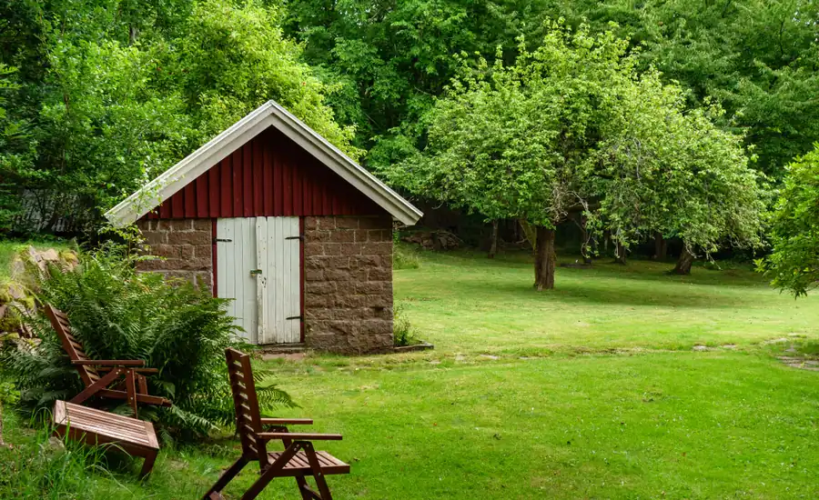 Kleines Gartenhaus mit rotem Dach steht direkt auf der Rasenfläche eines Gartens