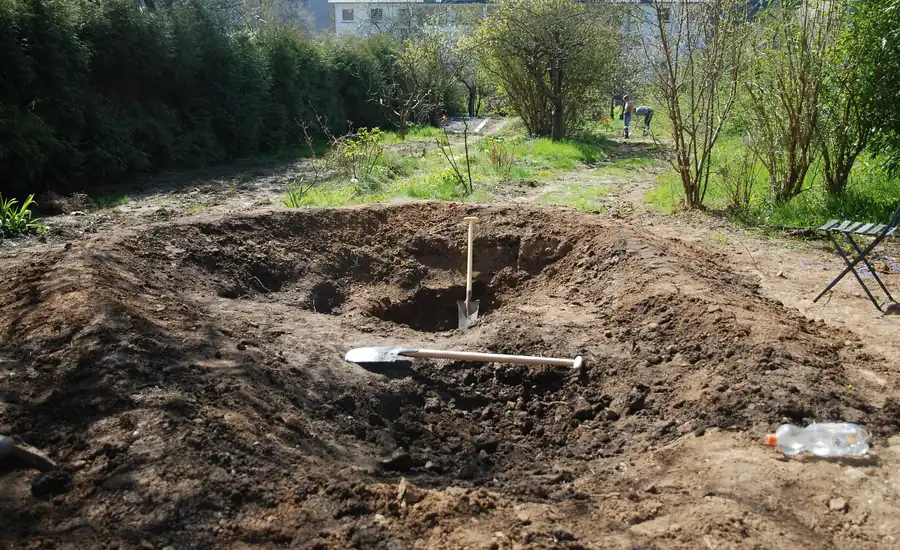 Ausgehobene Grube für einen Gartenteich mit aufgeworfenem Erdaushub
