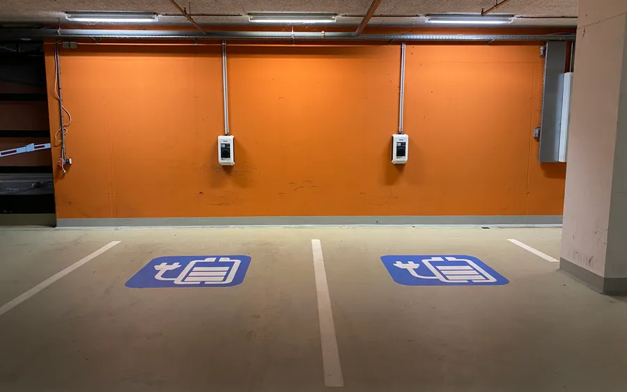 Tiefgarage mit zwei Wandladestationen an einer orangefarbenen Wand, davor zwei Stellplätze mit blauen Ladesymbolen auf dem Boden