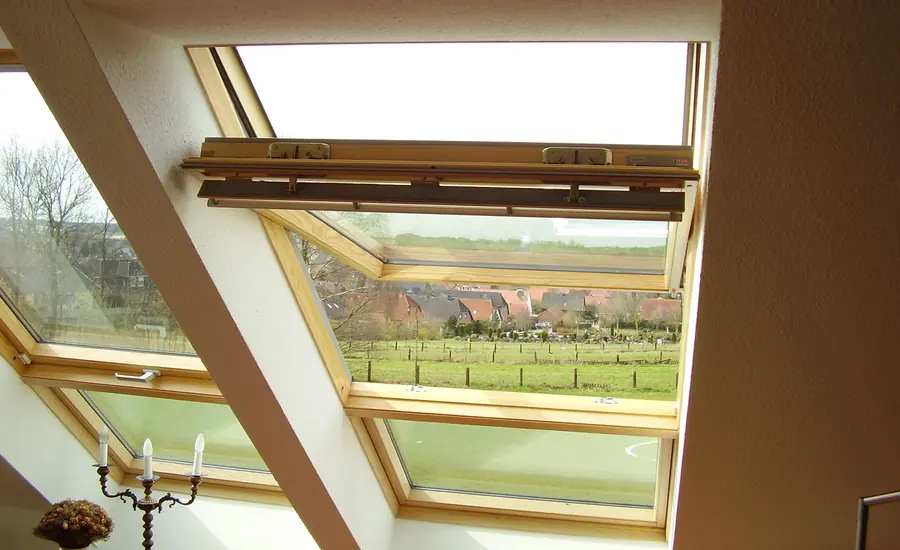 Weit geöffnetes Dachflächenfenster in einer Dachschräge mit Blick auf Wiesen und Bäume