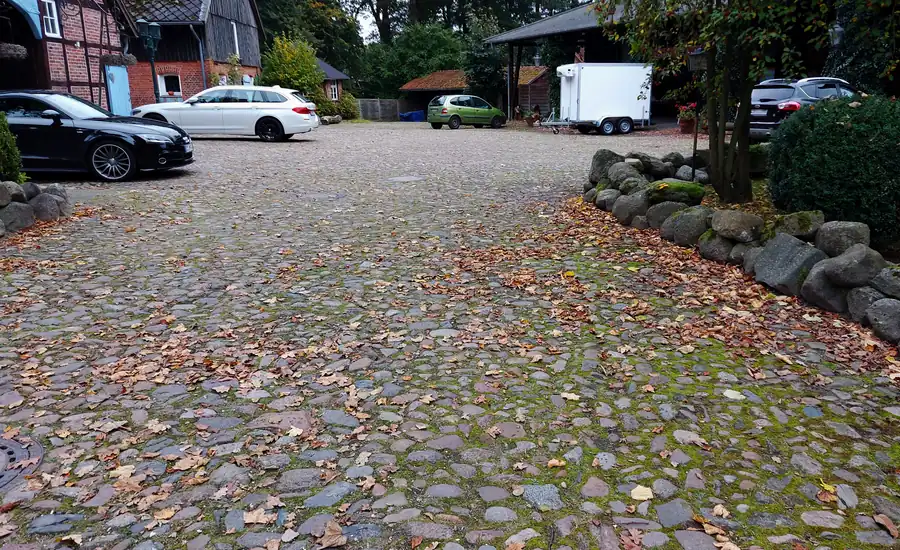Gepflasterte Hoffläche aus Natursteinen mit parkenden Fahrzeugen und Laub