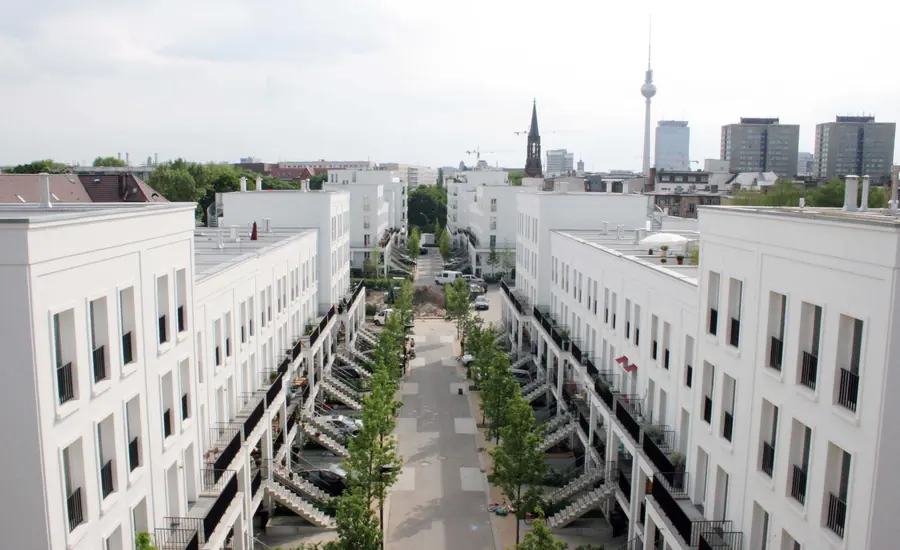 Straßenzug mit gleichartigen weißen Reihenhäusern, im Hintergrund die Berliner Skyline