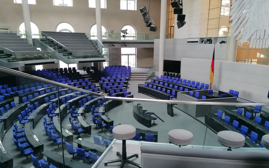 Leerer Plenarsaal des Deutschen Bundestags mit blauen Sitzreihen, Rednerpult, Deutschlandflagge und Teil des Bundesadlers