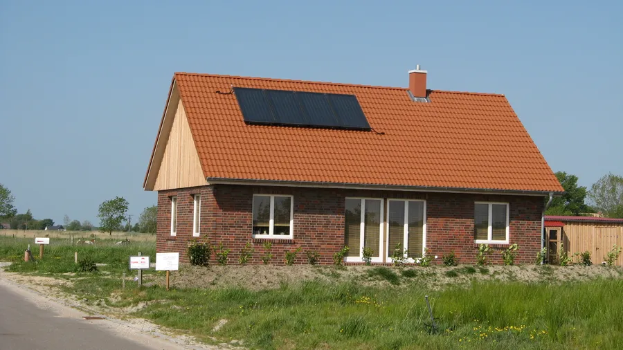 Neu gebautes Einfamilienhaus mit rotem Ziegeldach, auf dem ein Feld aus vier dunklen Solarmodulen liegt; Symbolbild