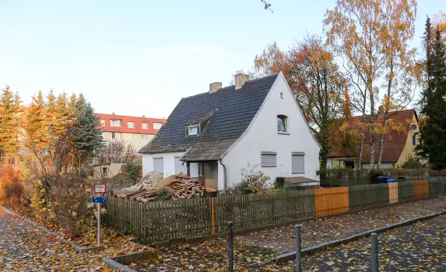 Älteres Einfamilienhaus mit steilem Satteldach hinter einem Holzzaun, davor Herbstlaub auf dem Gehweg in Köthen