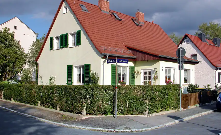 Doppelhaus aus den 1930er-Jahren mit roten Dächern, grünen Fensterläden und Hecke an einer Straßenecke in Dresden