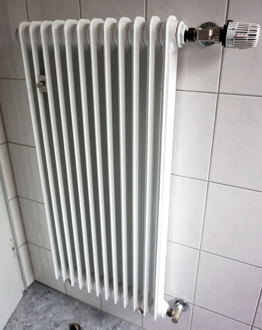 Weißer Röhrenheizkörper mit Thermostatkopf an einer gefliesten Badezimmerwand
