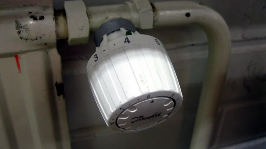 Weißer Thermostatkopf der Marke Danfoss an einem Heizkörper, Einstellskala von 2 bis 5; Symbolbild für Heizkosten