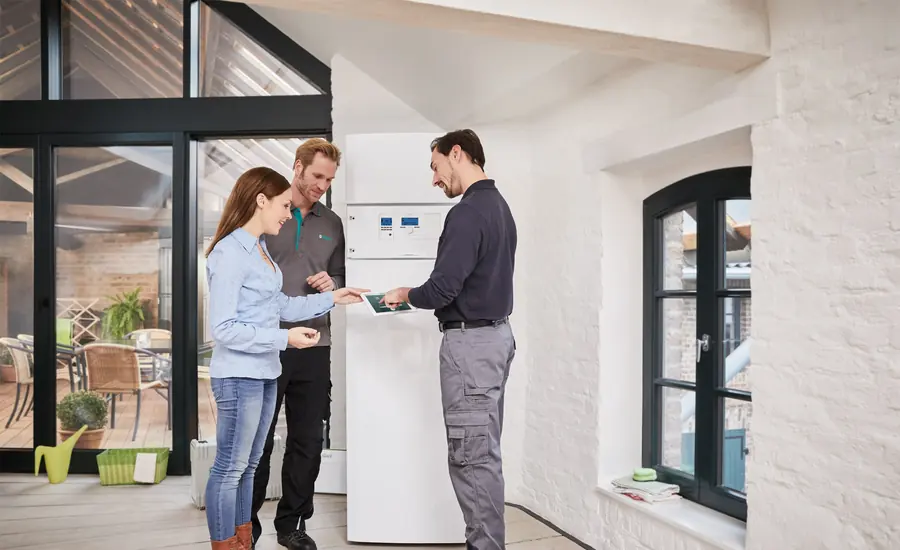 Paar im Gespräch mit einem Installateur vor einer Wärmepumpen-Inneneinheit