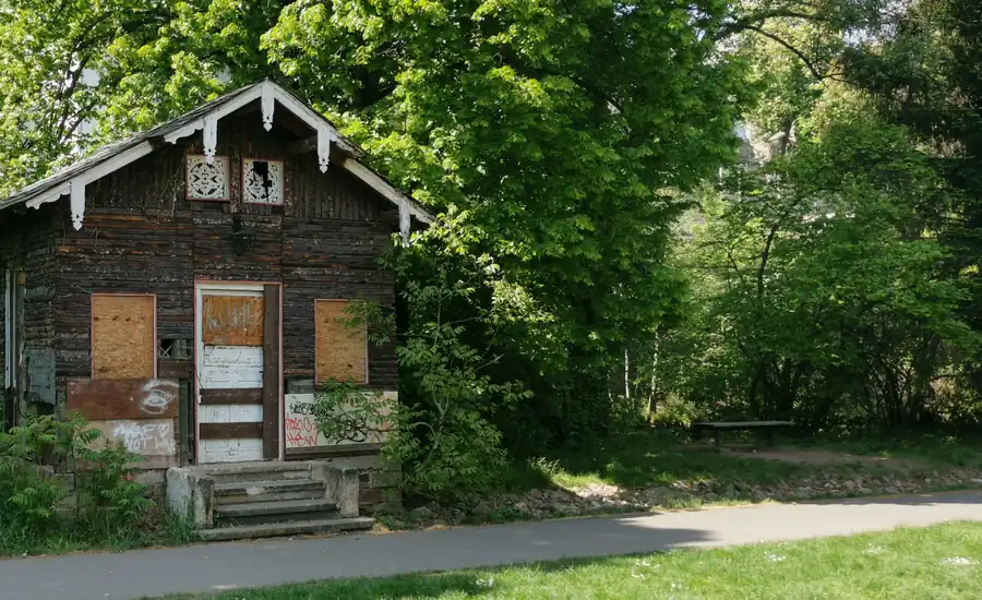 Älteres Gartenhaus aus Holz mit vernagelten Fenstern am Rand eines Weges